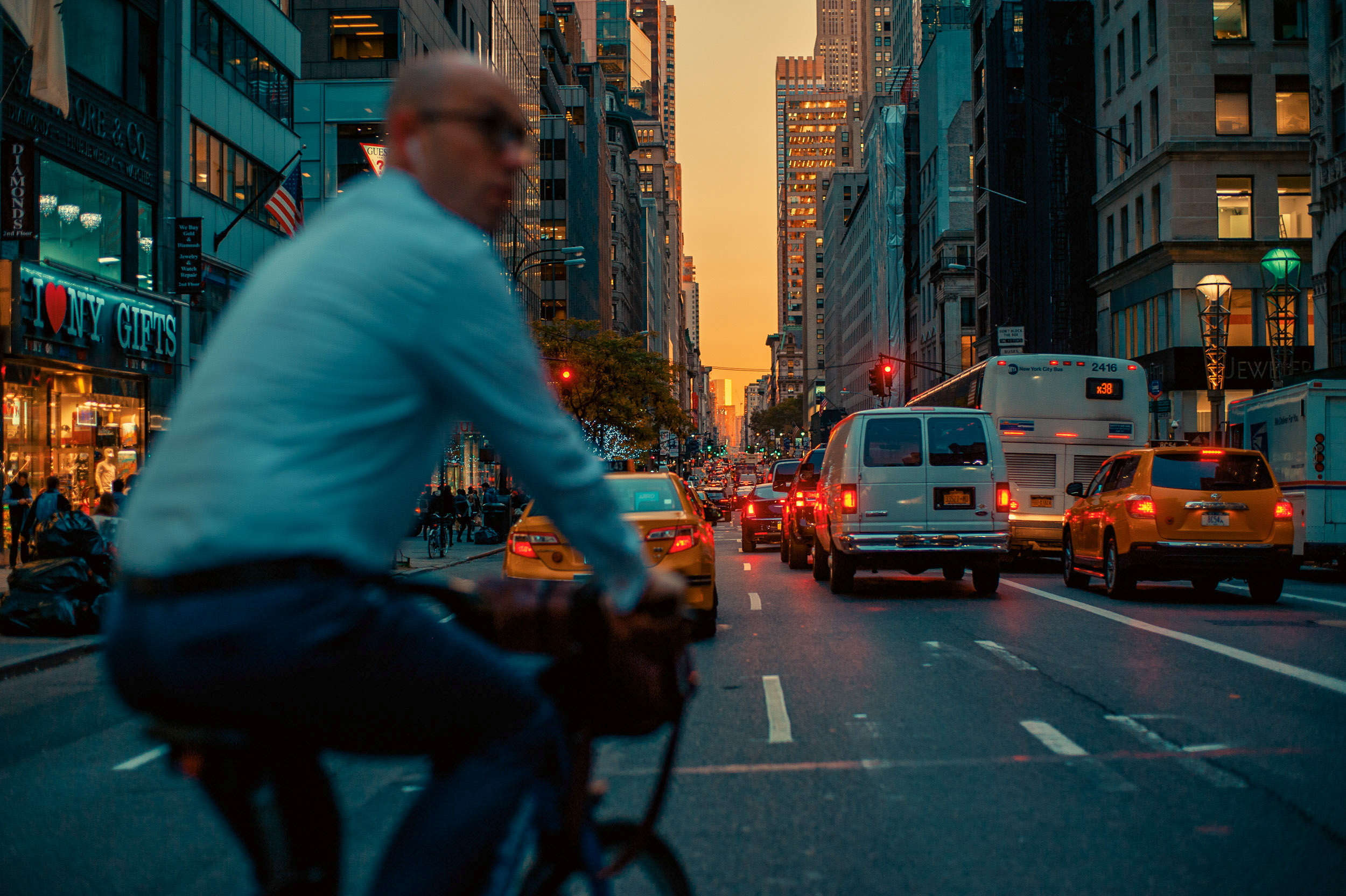 A MAN RIDES HIS BIKE THROUGH MIDTOWN MANHATTAN IN FRONT OF A BEAUTIFUL SUNSET