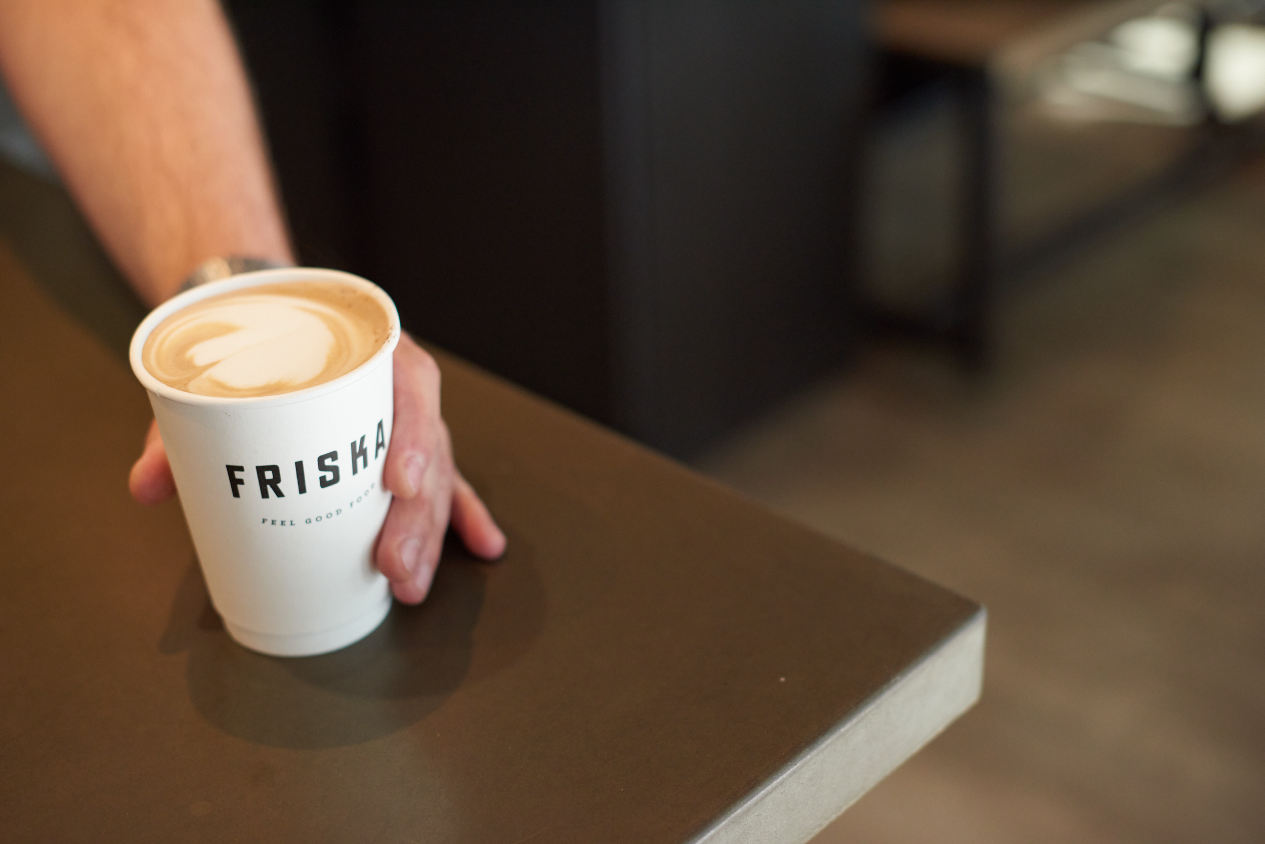 A CLOSE-UP OF A COFFEE CUP WITH A FRISKA LOGO EMBEDDED