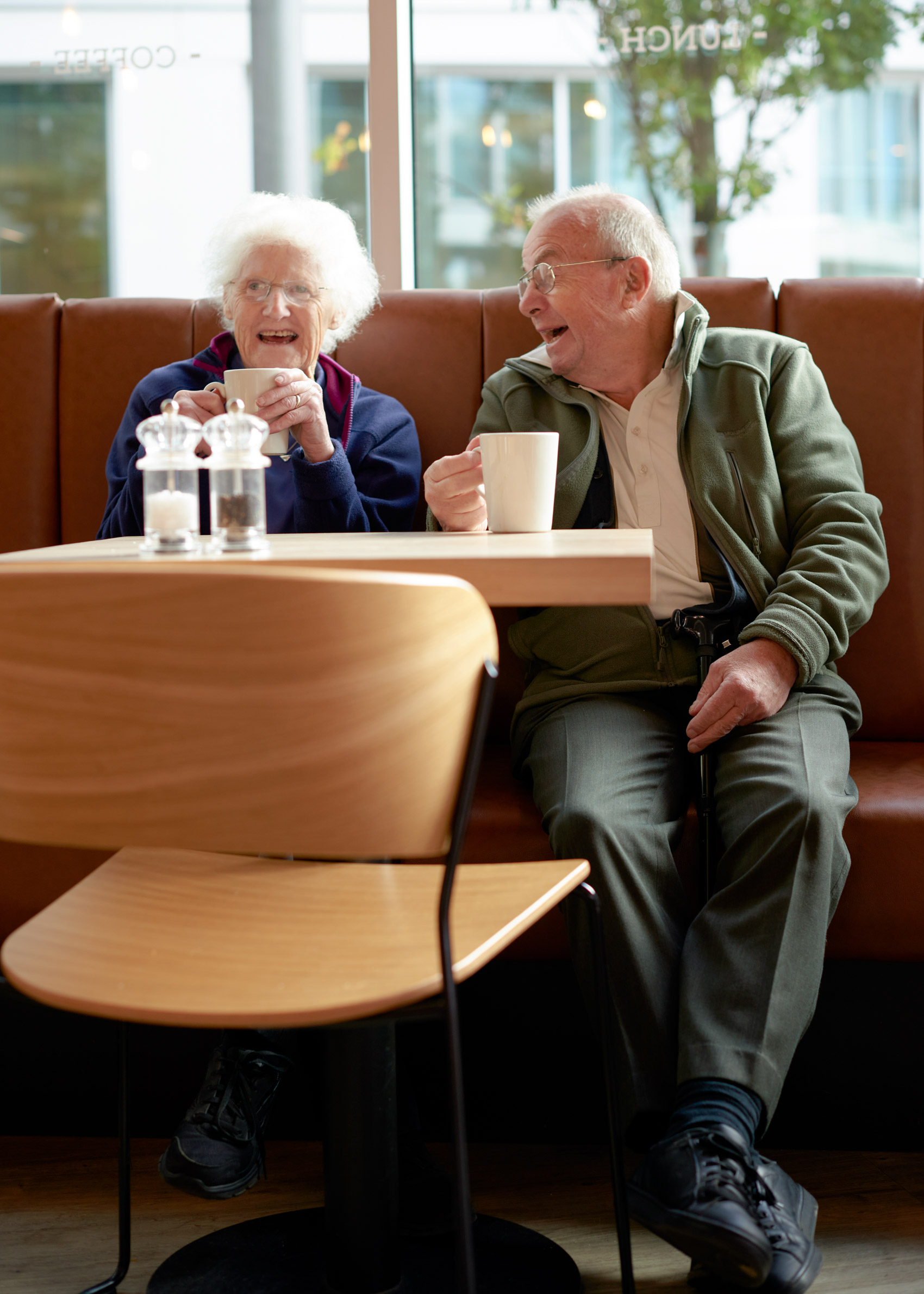TWO SENIORS E DRINK THEIR COFFEE AND LAUGH AT A RESTAURANT IN BRISTOL LONDON
