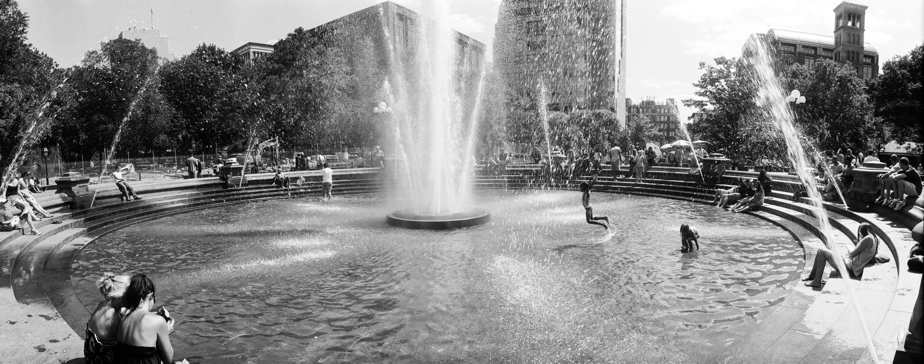 A panoramic photo of children playing  Washington Square Park in the summer of New York City