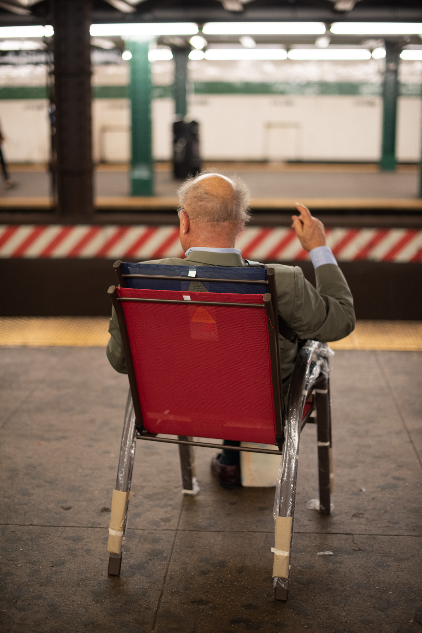 AN OLD MAN SITS IN HIS NEWLY PURCHASED CHAIR ON THE SUBWAY PLATFORM IN NEW YORK CITY