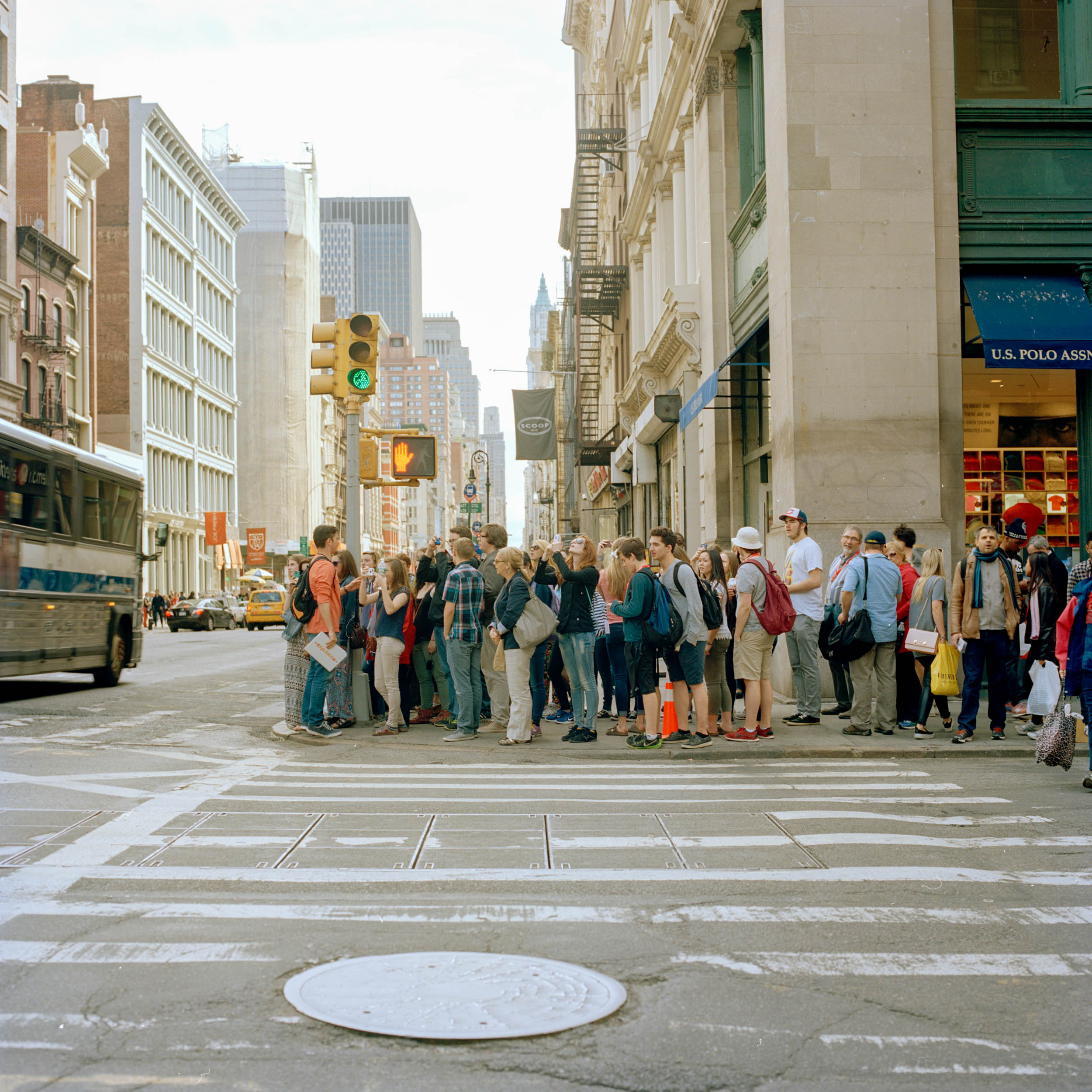 A CROWD OF TOURISTS GATHER AT THE CROSSWALK IN SOHO NEW YORK CITY