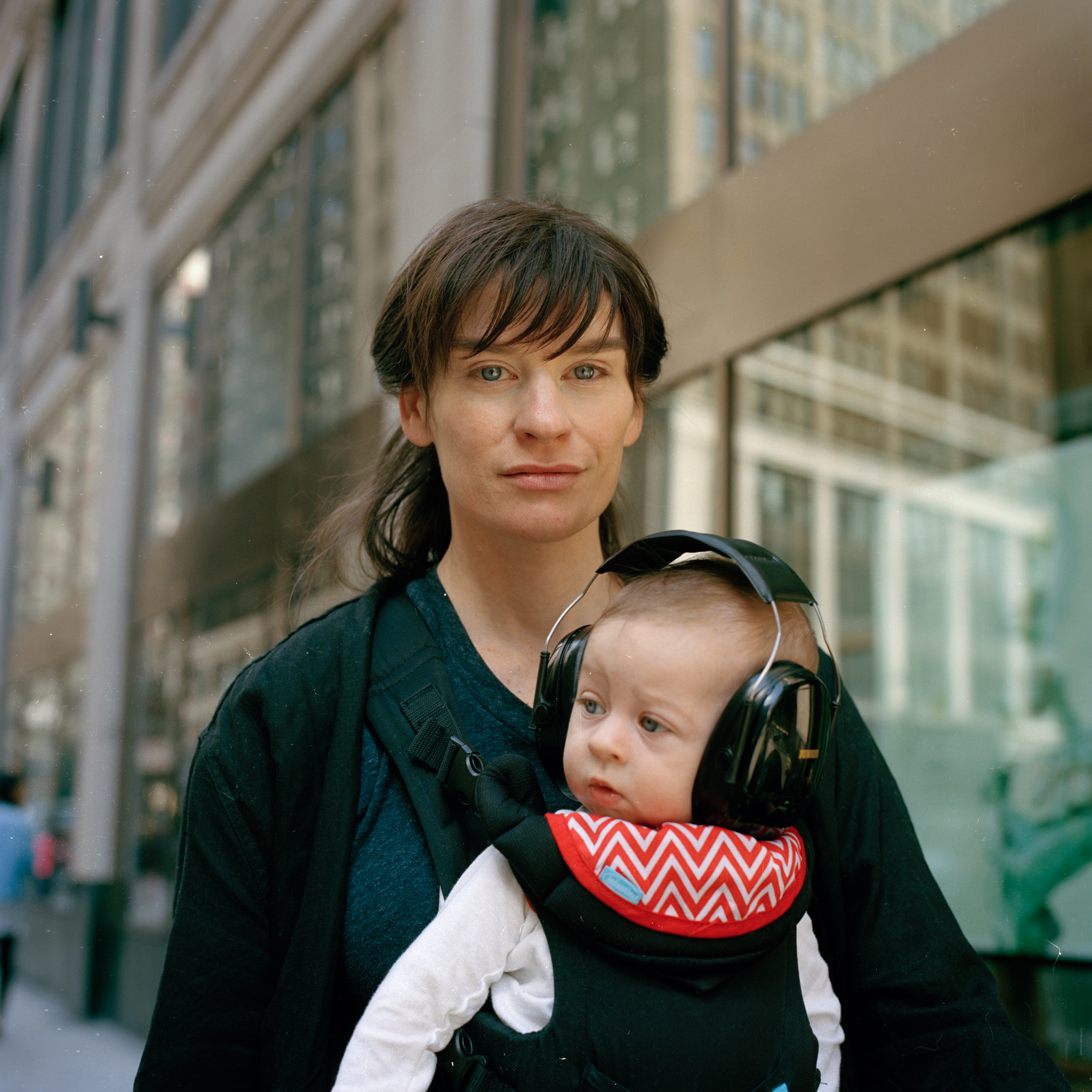 A WOMAN POSES FOR A STREET PORTRAIT WITH HER CHILD STRAPPED TO HER CHEST