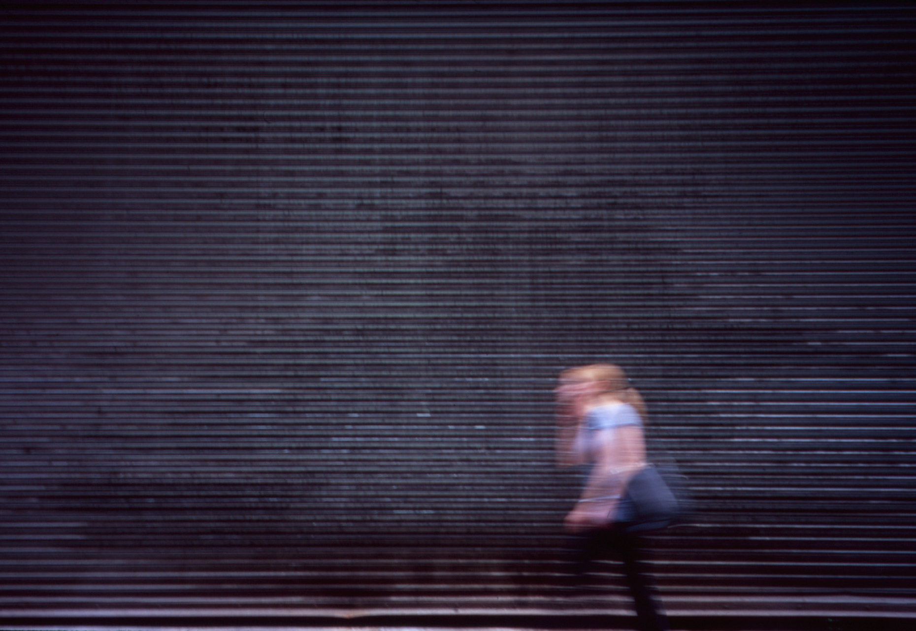 A woman on her phone strolls past some steel shutters in New York City. 